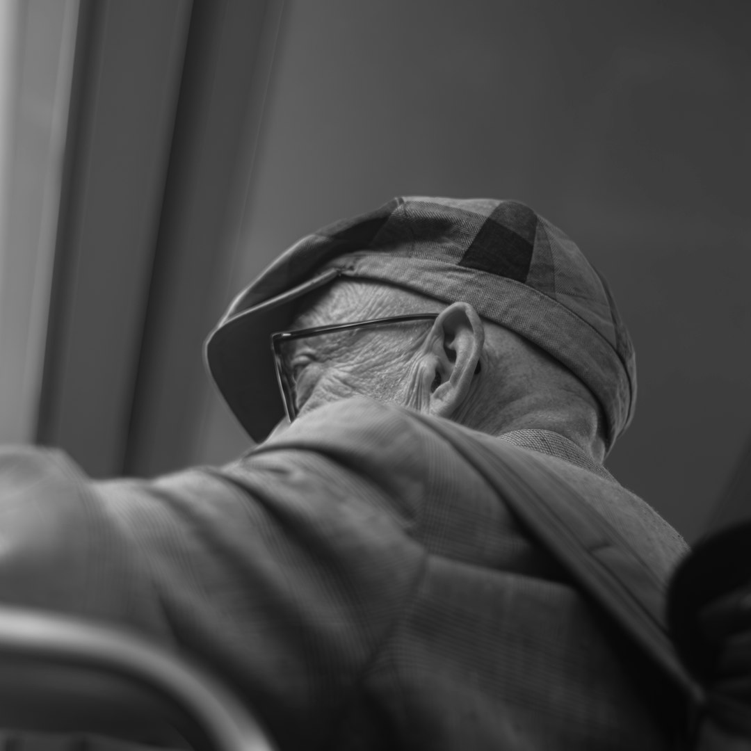 An elderly man wears a hat and glasses